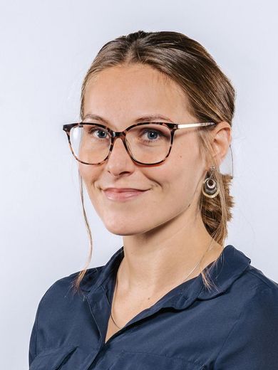 Auf dem Bild ist Johanna Günter zusehen. Sie hat ihre blonden Haare zu einem tiefen Zopf zusammengebunden. Sie trägt eine Brille und eine dunkelblaue Bluse. 